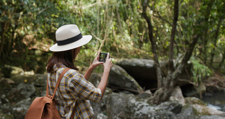 Fototapeta na wymiar Woman goes hiking, use cellphone for take photo in forest