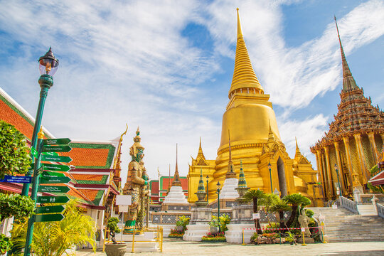 A demon guardian statue with a Great golden stupa in Wat Phra Kaew against the sky, Temple of the Emerald Buddha Wat Phra Kaew is one of the most famous places in Bangkok, Thailand - Powered by Adobe