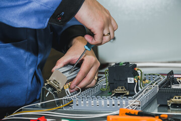 Electrician builder at work inspecting cabling connection of high voltage power electric line in industrial distribution fuseboard. Male hand with screwdriver fixes cable in electric transformer