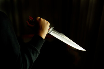 Close-up of a hand holding a large knife in a dark room. Concept of crime and violence.