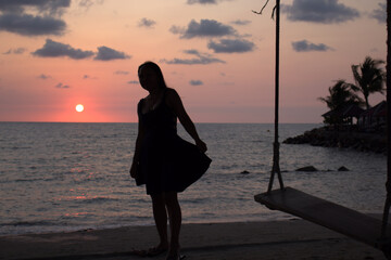 Silhouette of a lady in a pretty dress at sunset on tropical island at sunset