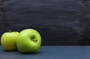 Couple of bright green apples on dark blue desk with blackboard texture in background. Copy space, close-up. School snacks or organic food concept