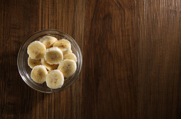 Bananas cut in a glass bowl on a wooden table. Top view, copy space