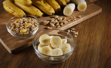 A banquet of bananas with granola and cereal on the wooden background and a cut banana in a glass bowl on a table