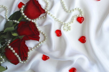 three red roses lie on a white shade from satin with hearts