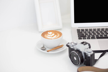 cup of coffee on white desk with camera and laptop in room.