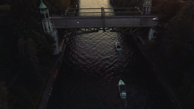 Drone Following Boats Cruising Montlake Cut Under Bridge with People Driving Cars at Sunset in Seattle