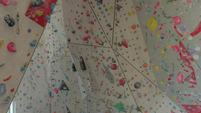 DRONE: Flying around an empty indoor rock-climbing training center closed due to the covid-19 outbreak. Aerial view of the high walls of a climbing gym filled with colorful magnesium-covered holds.