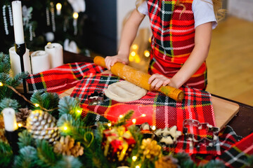 A child in a chef's hat and apron prepares cookie dough for Christmas. Children prepare sweets in the kitchen with a Christmas tree on a snowy winter day.