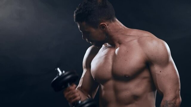 Fit and sporty bodybuilder over black background. Bodybuilder training using dumbbells. Sport and fitness.