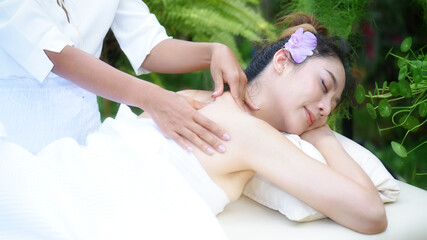 Young woman receiving back massage at spa in the garden. Professional masseuse working with her...