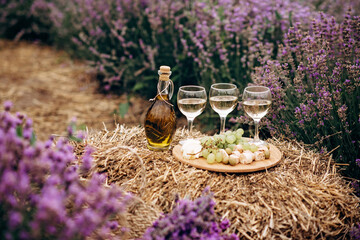 Three glasses of white wine, appetizers cheese, grapes, biscotti, olive oil and a bouquet of flowers on a haystack among lavender bushes. Romantic picnic. Soft selective focus. © Tasha Sinchuk
