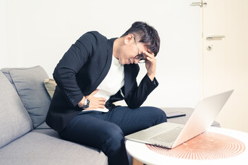 Young Asian business man sitting on sofa and working from home. Man feeling stress and suffering from office syndrome with headache. Tired young entrepreneur manager. Work from home concept