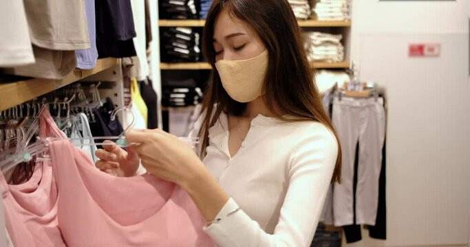 Young asian woman wearing mask choosing clothes in shopping mall.