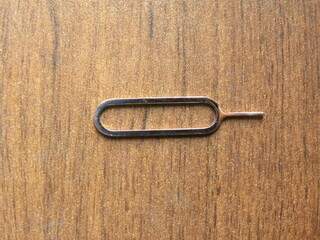 Small steel SIM card tray opener pin kept on wooden table