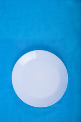 Empty clean white porcelain plate stands on a blue background. Dishes. Vertical