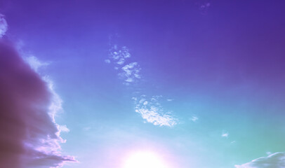 green purple light on blue sky with soft clouds and bright sun