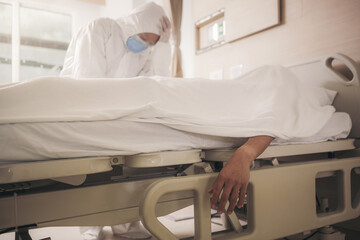 Doctor in protective suit, sadness and depressed beside Coronavirus victim body on bed after the...
