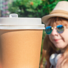 Takeaway coffee in the summer. A cup for coffee is shown on the background of a girl. There is a place for text.