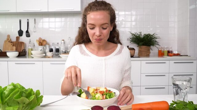 Beautiful young woman eating salad in the kitchen.