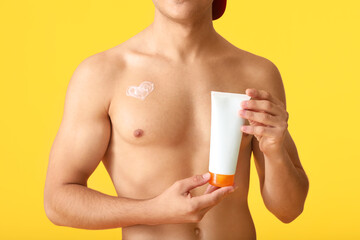 Young man with sun protection cream on color background