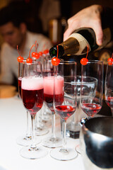 The waiter pours champagne into the glasses. On the edge of the glass is a cherry. Sparkling wine at a party.