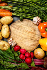 Frame made of fresh assorted vegetables around wooden round cutting board close up