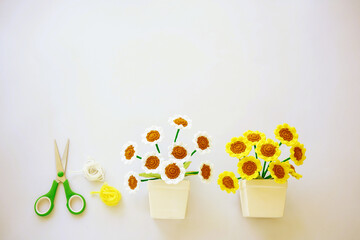 White and yellow sun flowers in vases made by cotton threads.  A scissors with green is placed by yarns.  Handcraft, art objects are for leisure and decoration. copy space