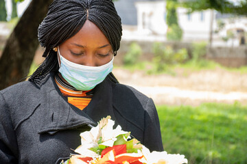 african woman mourning, wearing black and holding flowers