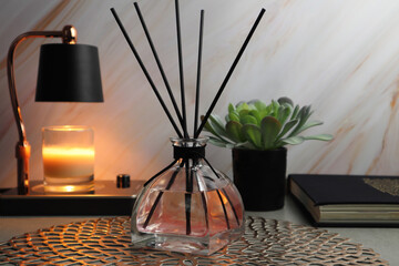 Fototapeta na wymiar luxury aromatic reed diffuser glass bottle and candle warmer and book and small plant display on the grey table with background of marble wall in the bedroom