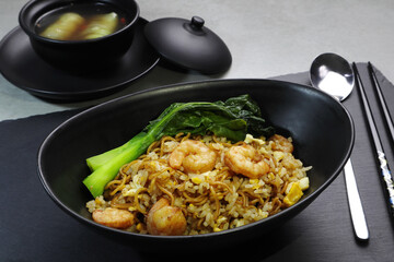 fried rice and instant noodles with shrimps and cantonese kale in the black bowl served on the black plate together with vegetable soup on the grey table in the restaurant