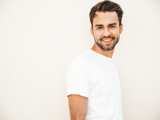 Portrait of handsome smiling stylish hipster lambersexual model.Man dressed in white T-shirt. Fashion male posing on the street background near wall in round sunglasses
