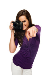 Click! Young beautiful woman photographer taking images with digital camera and pointing to camera. Isolated on white.