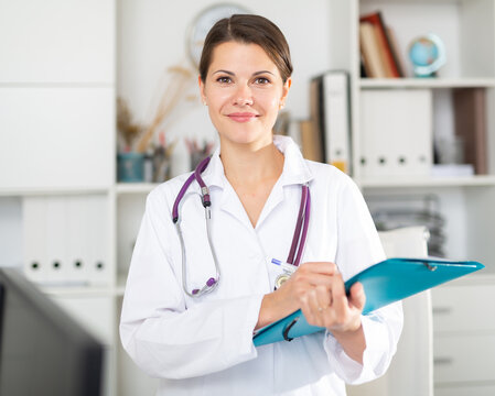 Polite female doctor meeting patients in medical office, filling out medical form on clipboard