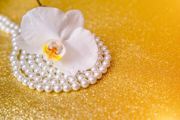 White Orchid and pearl necklace on a shiny gold background
