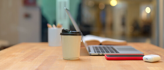 Study table with laptop, smartphone, paper cup, stationery and opened book in library