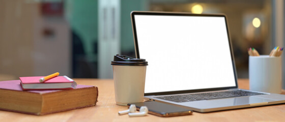 Study table with books, mock up laptop, smartphone, earphone, stationery and paper cup