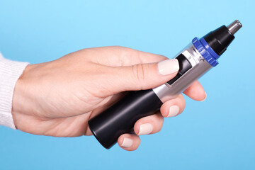 Hand with nose trimmer, hair electric cutter. Isolated on blue background.