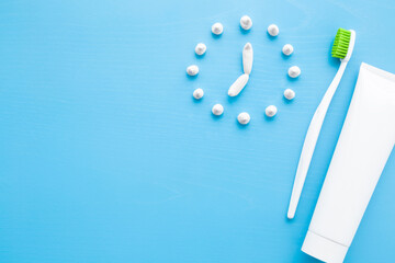 Toothbrush with green bristles and white tube of toothpaste on pastel blue table background. Clock created from paste. Healthy teeth. Morning routine concept. Empty place for text. Top down view.