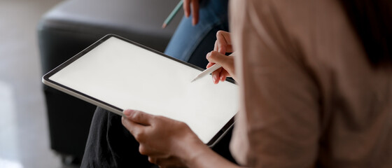 Female using mock up tablet with stylus pen while sitting on sofa in living room