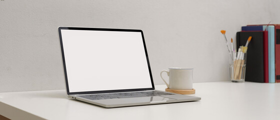 Simple workspace with mock up laptop, cup, copy space painting brushes and books on white table