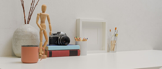Modern workspace with copy space, mug, painting tools, camera, books and decorations
