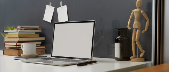 Study table with mock up laptop, stack of books and decorations on white desk