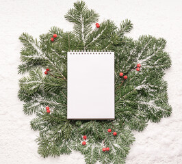 Fototapeta na wymiar Fluffy green branches of spruce blank paper notepad on a white wooden background. Horizontal frame flat layout.