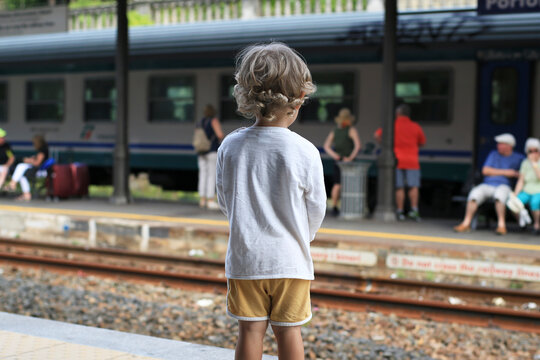 Beautiful curly-haired boy at the station looks at the train
