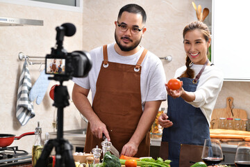Young Asian couple blogger vlogger and online influencer recording video content on healthy food in the kitchen.