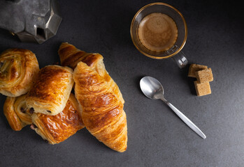 Breakfast with croissants, cinnamon buns and chocolate cookies, fresh orange juice and coffee on the side on a dark background in a spot light.