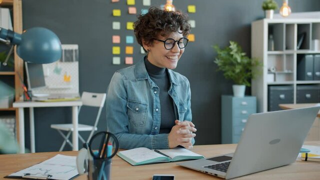 Slow motion of joyful business lady speaking on video call with laptop in workplace communication online smiling and gesturing waving hand. People and computers concept.