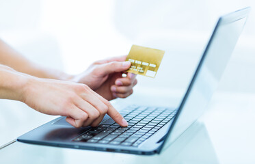 Close-up of persons hands typing and paying using a laptop computer while holding a credit card. Online banking, booking and shopping concept. 
