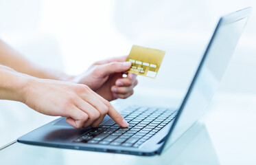 Close-up of persons hands typing and paying using a laptop computer while holding a credit card....